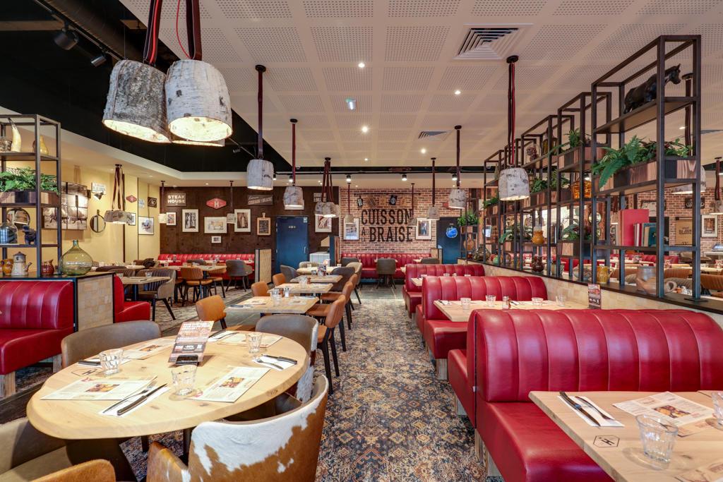 Un restaurant Hippopotamus à l'intérieur chaleureux avec des banquettes rouges, des tables en bois, des chaises colorées, des suspensions lumineuses, des photos encadrées et des plantes en pot.