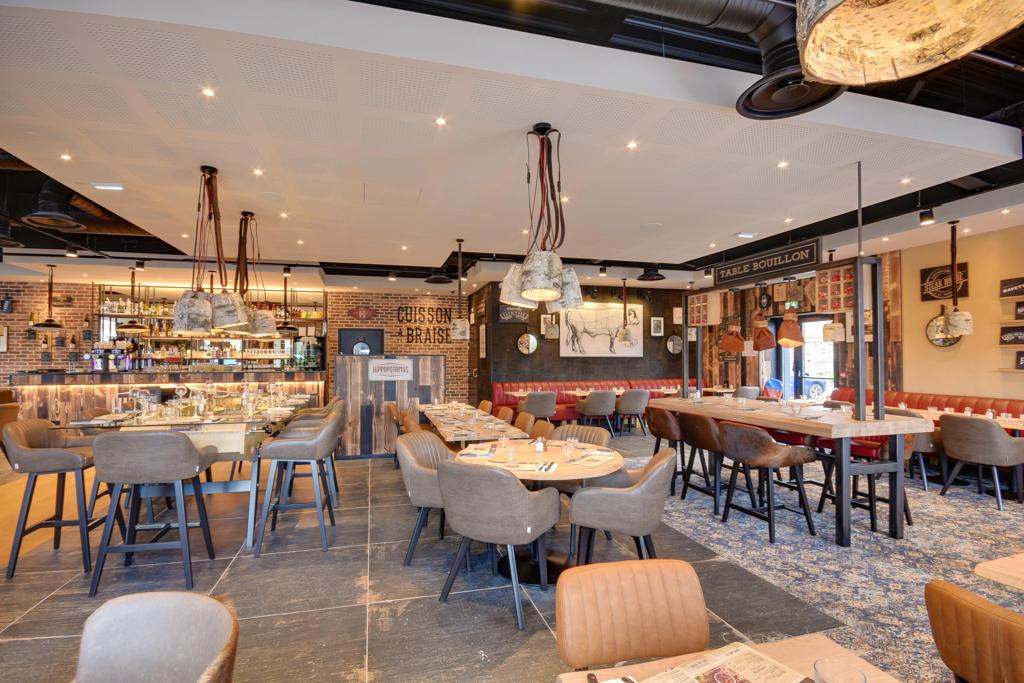 Intérieur de restaurant Hippopotamus confortable avec tables en bois, chaises rembourrées, bar bien approvisionné, éclairage chaleureux et murs en briques décorés.