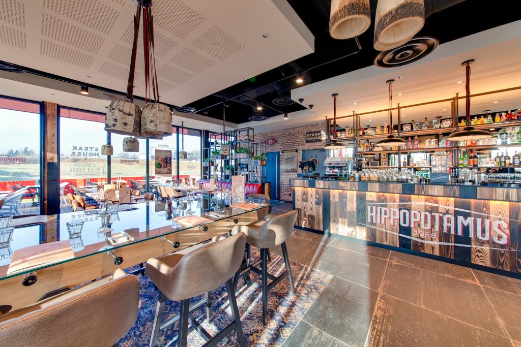 Intérieur moderne d'un restaurant Hippopotamus avec des tables en bois élégantes, des chaises rembourrées, des tapis à motifs et un bar moderne en bois