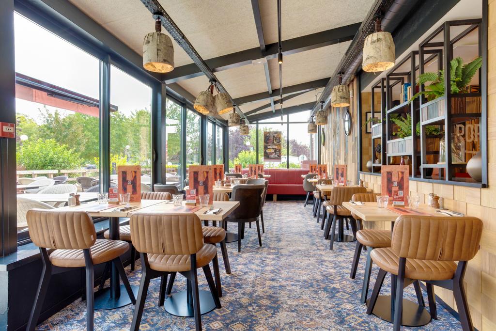 Intérieur de restaurant Hippopotamus confortable avec une décoration moderne, des chaises rembourrées marron, des tables en bois, de grandes fenêtres et des suspensions décoratives.