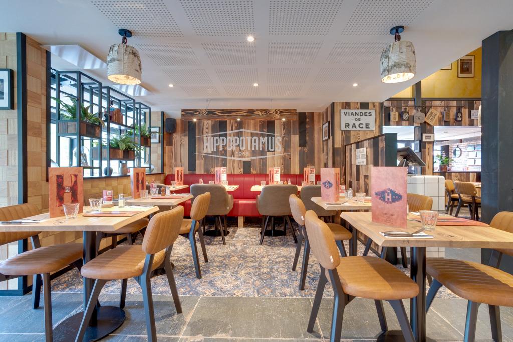 Intérieur moderne avec tables en bois, chaises rembourrées et banquette rouge centrale. L'éclairage d'ambiance et les décorations murales embellissent l'espace.