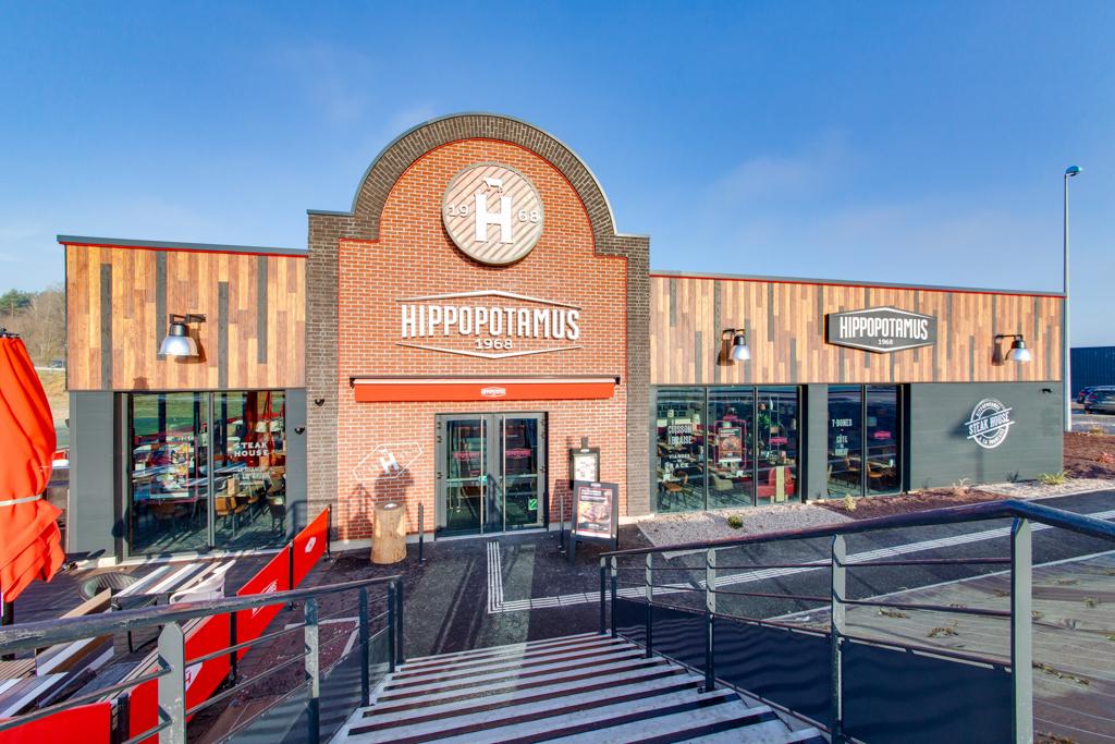 Vue extérieure d'un restaurant Hippopotamus à Epinal avec une façade en briques, de grandes fenêtres et des accents en bois sous un ciel bleu clair.