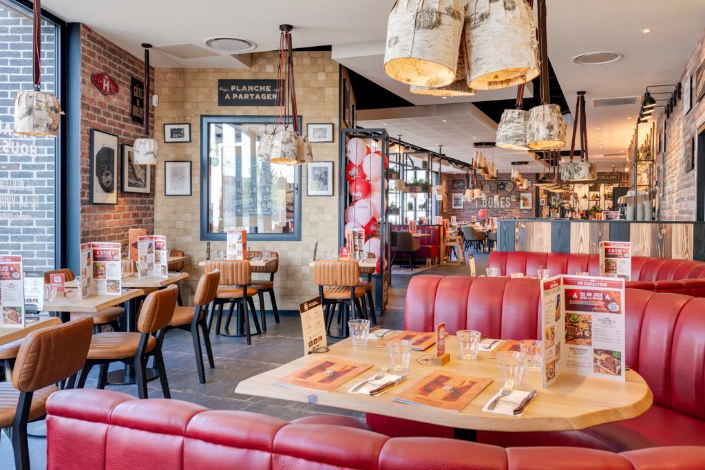 Intérieur d'un restaurant Hippopotamus chaleureux avec des sièges rouges et beiges, des tables en bois, des luminaires originaux et des menus sur les tables, créant une atmosphère accueillante.
