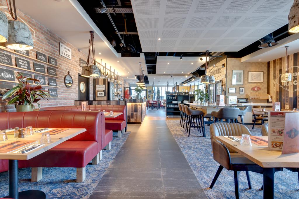 Intérieur moderne de restaurant Hippopotamus avec banquettes rouges, tables en bois, décorations murales et plantes. Éclairage lumineux et mélange de briques apparentes et de murs en bois.
