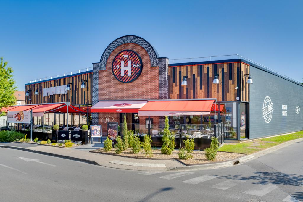 Vue d'un restaurant Hippopotamus avec des auvents rouges au-dessus d'une terrasse extérieure, doté d'une façade en briques et d'éléments décoratifs en bois.