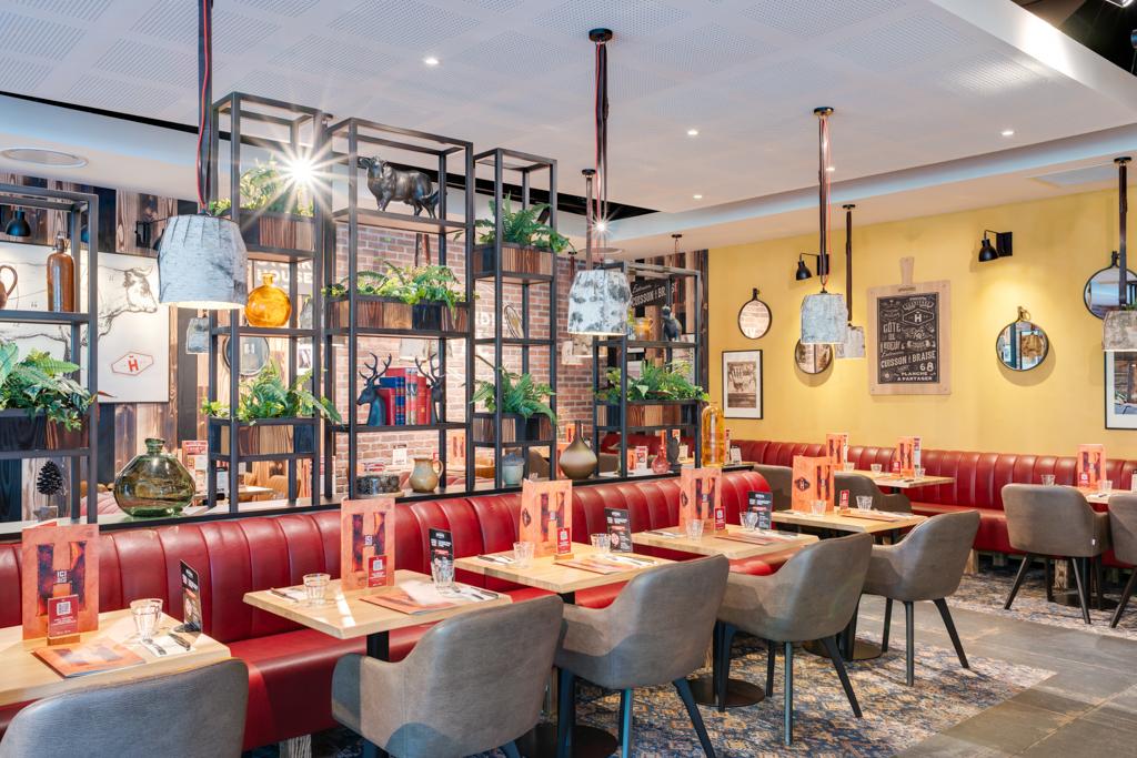 Intérieur moderne d'un restaurant Hippopotamus avec des murs jaunes, des banquettes rouges, des tables en bois, des chaises grises et des étagères décoratives avec des plantes et divers objets.