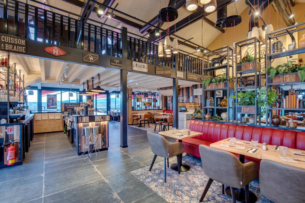 Un restaurant Hippopotamus moderne avec des banquettes rouges, des tables dressées, une décoration industrielle, des plantes et une mezzanine