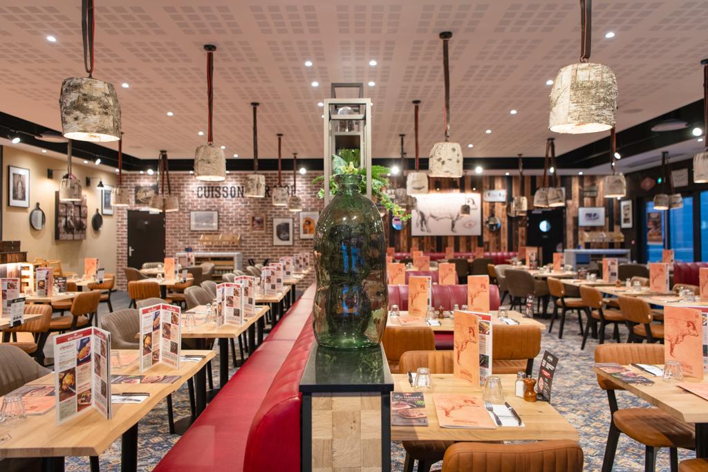 Intérieur spacieux d'une restaurant Hippopotamus avec tables en bois, sièges rouges, lampes suspendues et accents de brique ; les menus et les plantes décoratives ajoutent des détails.