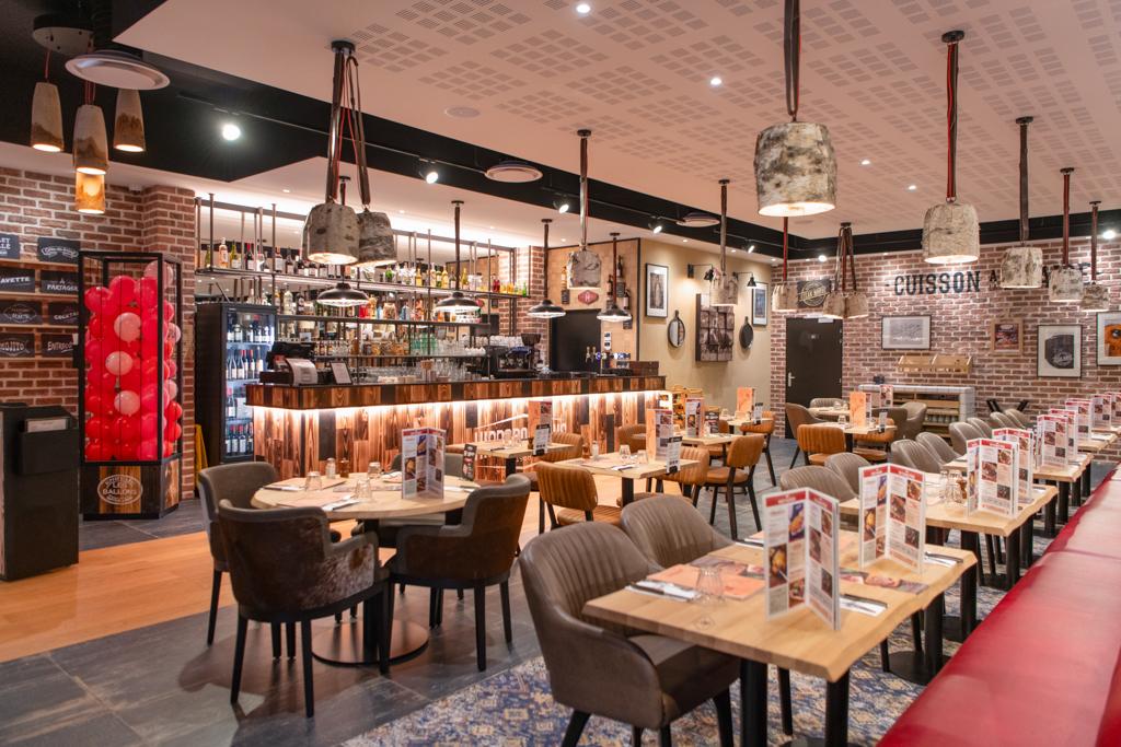 Intérieur d'un restaurant Hippopotamus chaleureux avec tables en bois, sièges moelleux, bar bien approvisionné et éclairage tamisé. Les murs en briques et les objets décoratifs renforcent l'ambiance.