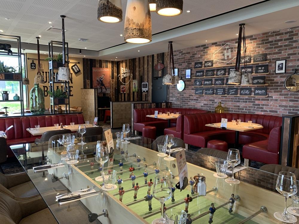 Un restaurant Hippopotamus confortable avec des banquettes rouges, des murs en briques, un baby-foot servant de table et un menu écrit à la craie sur le mur.