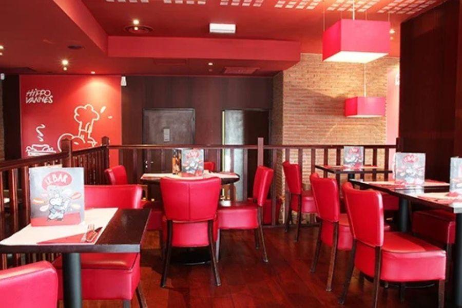 Un restaurant Hippopotamus à l'intérieur chaleureux avec des chaises rouges, des tables en bois, des murs en briques et des suspensions roses. Les menus sont disposés sur les tables.