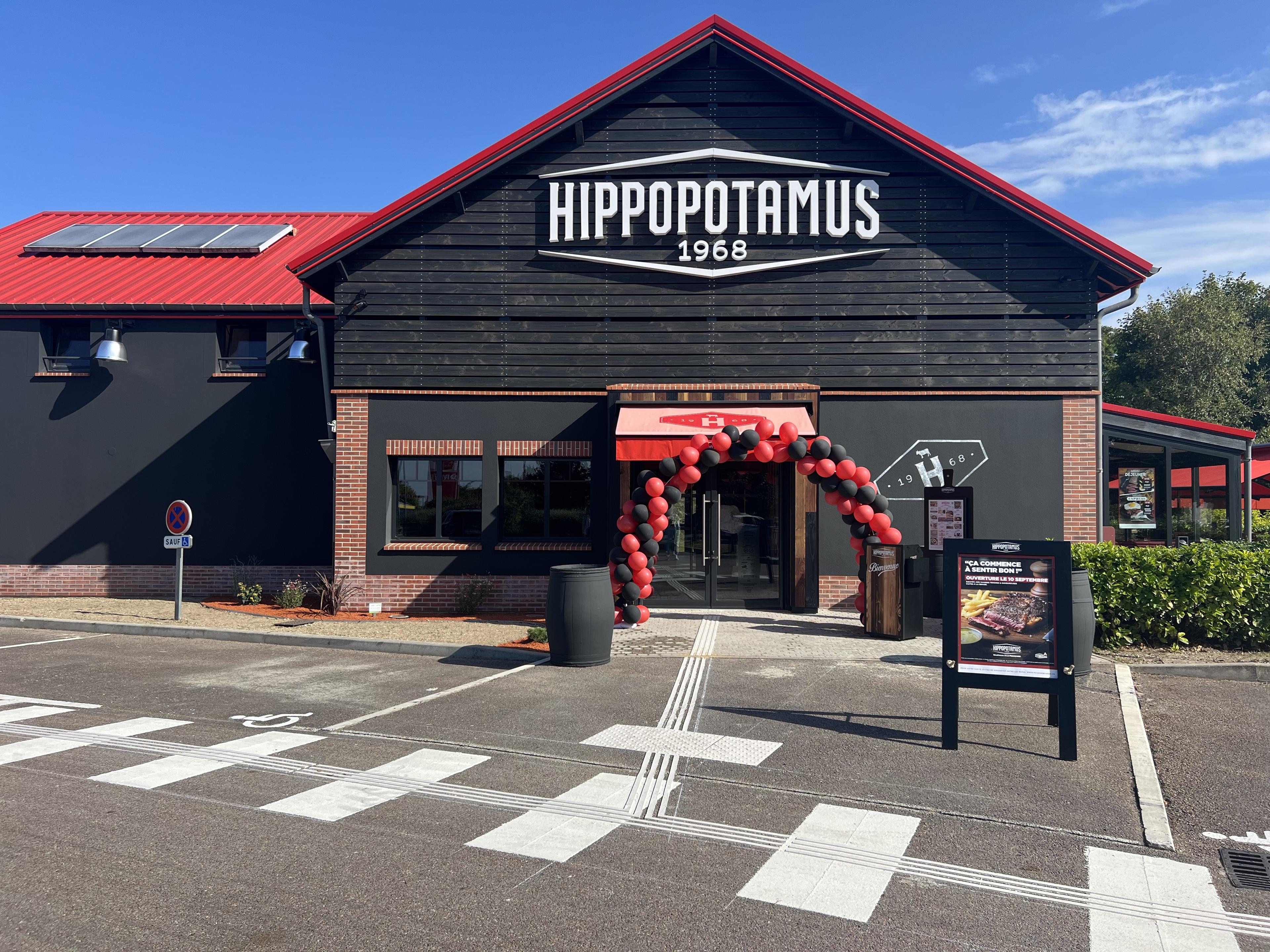 Vue de face d'un restaurant Hippopotamus avec une arche de ballons rouges et noirs à l'entrée, par une journée ensoleillée.