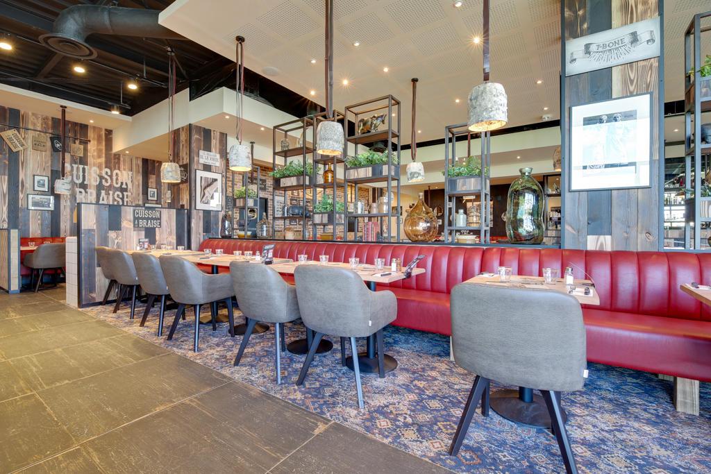 Intérieur moderne d'un restaurant Hippopotamus avec tables en bois, chaises rembourrées, banquettes rouges, étagères décoratives et grandes fenêtres laissant entrer la lumière naturelle.