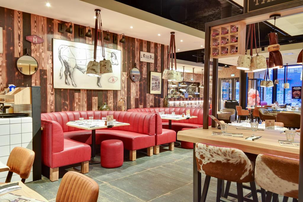 Intérieur de restaurant Hippopotamus chaleureux avec banquettes rouges, décor rustique, touches de cuir de vachette et éléments en bois. Tables dressées pour le dîner.