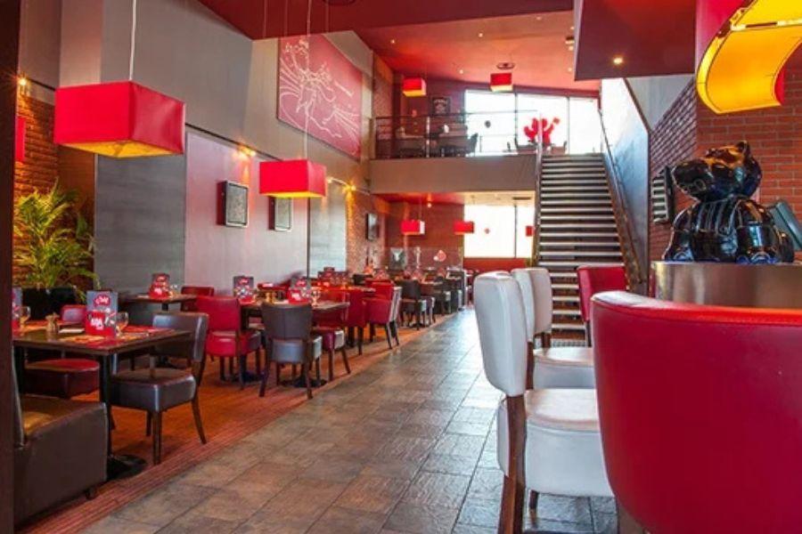 Intérieur moderne de restaurant avec une décoration rouge et blanche, des tables en bois, des chaises en cuir et un escalier menant à l'étage supérieur.
