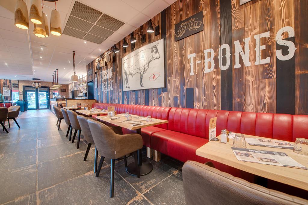 Intérieur chaleureux d'un restaurant Hippopotamus avec des sièges rembourrés rouges, des tables en bois, des plantes, des objets décoratifs et de grandes fenêtres donnant sur l'extérieur.