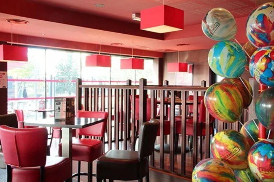 Un restaurant Hippopotamus lumineux avec une décoration, des chaises et des tables rouges. Des ballons colorés sont regroupés au premier plan, et de grandes fenêtres laissent entrer la lumière naturelle.