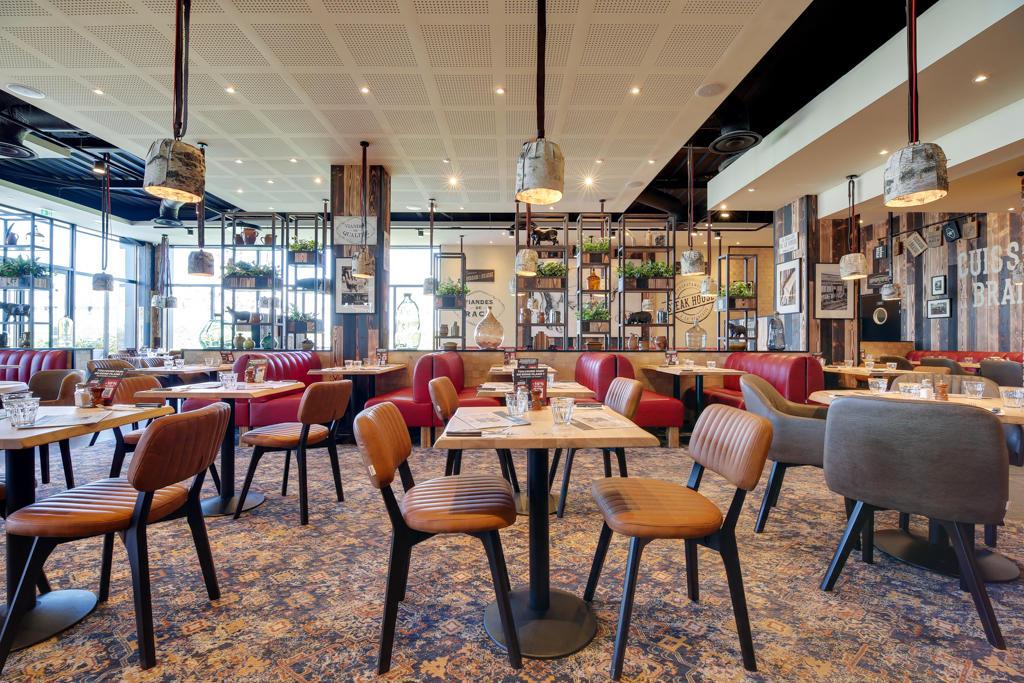 Intérieur moderne d'un restaurant Hippopotamus avec tables en bois, chaises rembourrées, banquettes rouges, étagères décoratives et grandes fenêtres laissant entrer la lumière naturelle.