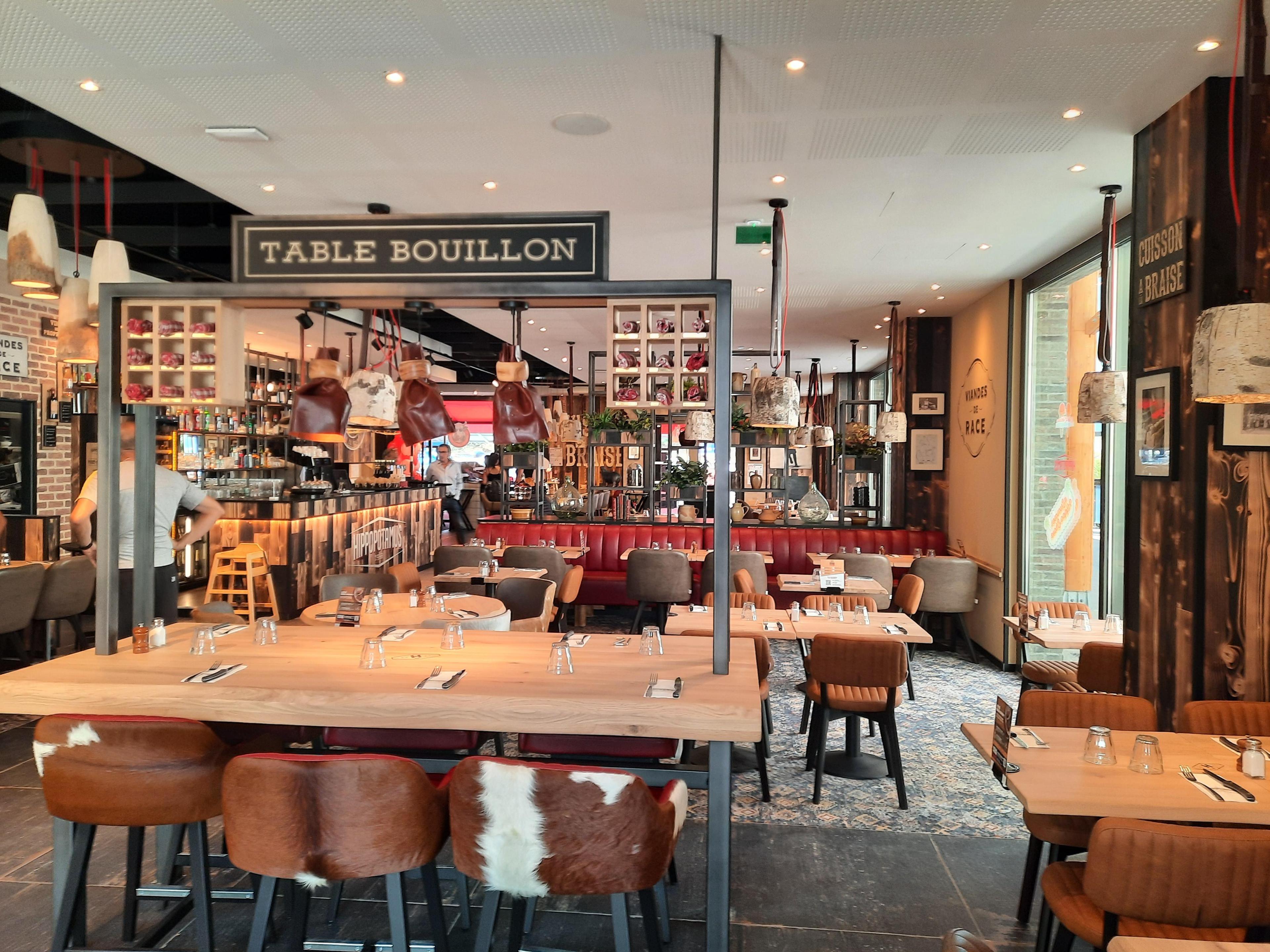 Intérieur chaleureux d'un restaurant de steakhouse Hippopotamus avec tables en bois, chaises en cuir et éclairage tamisé.