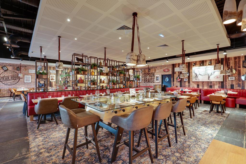 Intérieur moderne de restaurant Hippopotamus avec tables en bois, chaises en cuir et table haute centrale. Banquettes rouges et décorations murales en arrière-plan.