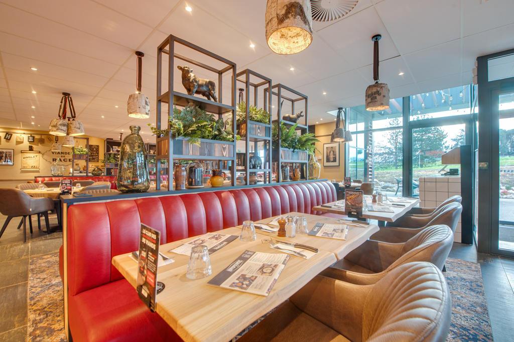 Intérieur chaleureux d'un restaurant Hippopotamus avec des sièges rembourrés rouges, des tables en bois, des plantes, des objets décoratifs et de grandes fenêtres donnant sur l'extérieur.