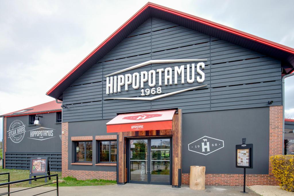 Grande façade extérieure d'un restaurant Hippopotamus Steakhouse, avec des briques et des panneaux sombres, rehaussée de touches de rouge.
