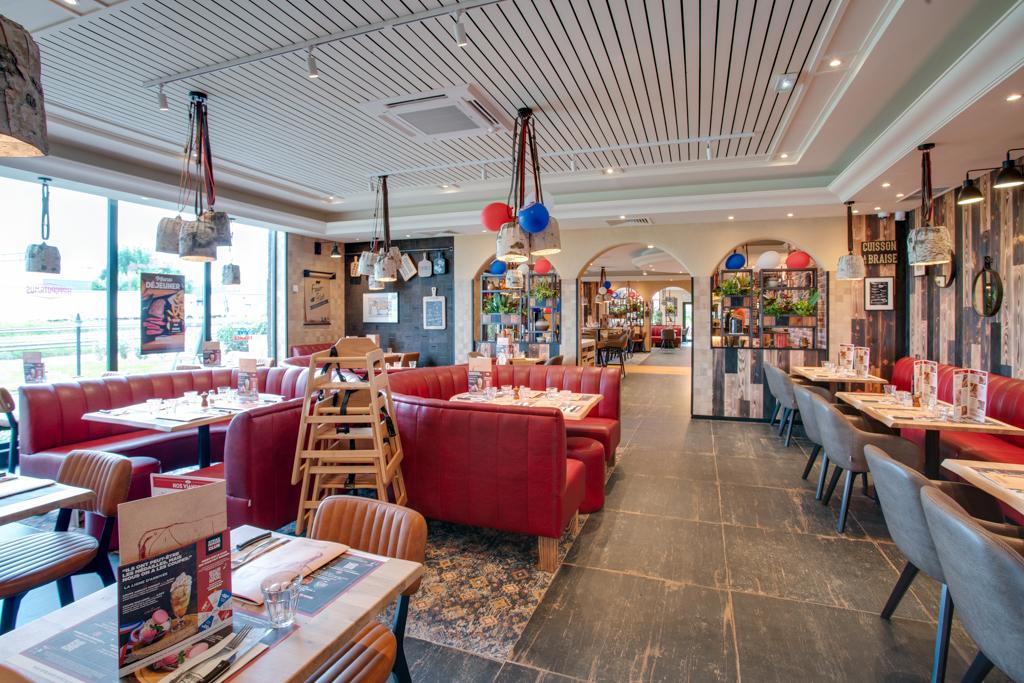 Intérieur lumineux du restaurant Hippopotamus avec des banquettes rouges, des chaises en bois et des décorations colorées. De grandes fenêtres et un sol à motifs créent une atmosphère accueillante.