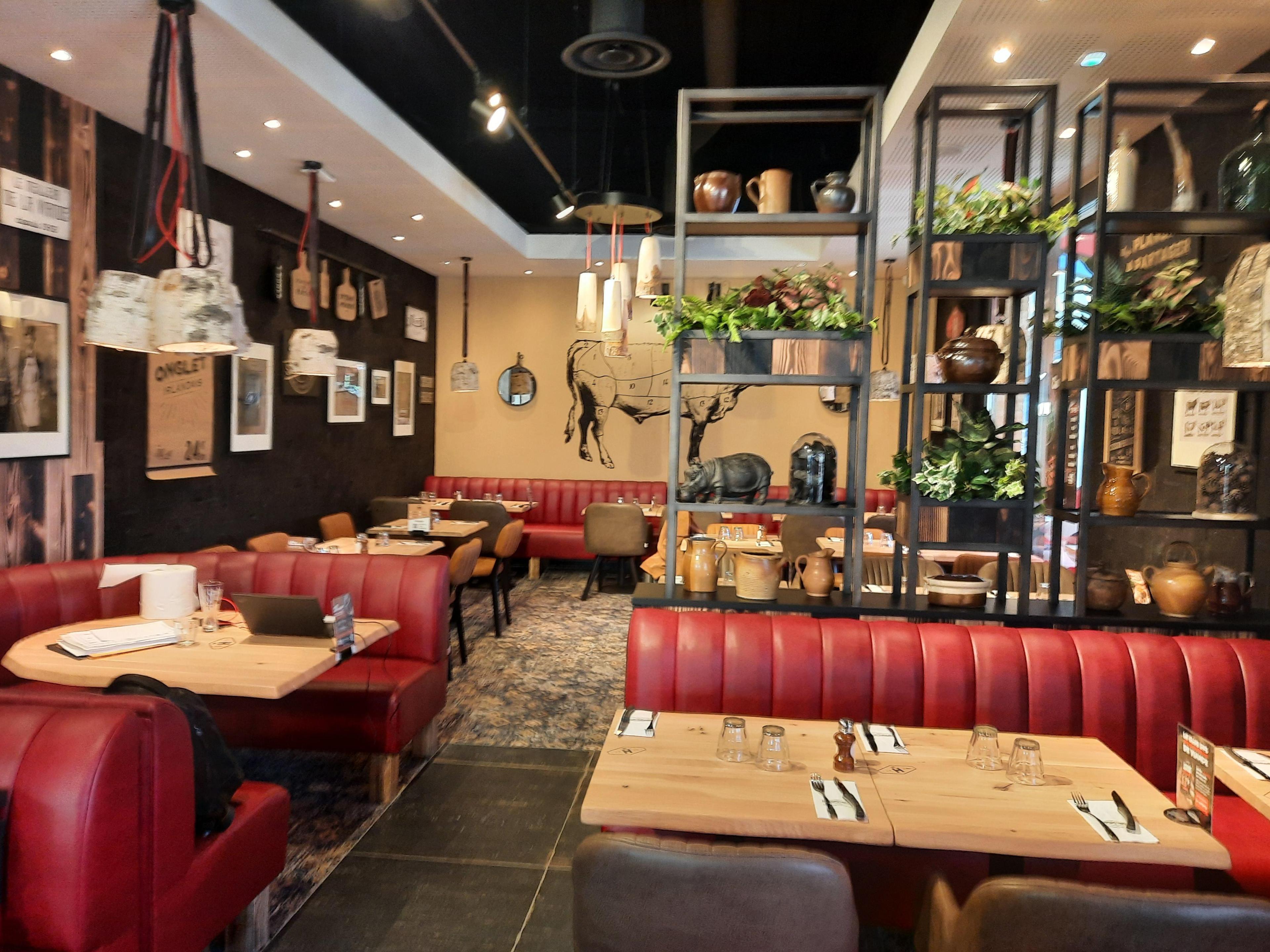 Intérieur chaleureux d'un restaurant Hippopotamus avec banquettes rouges, tables en bois, poteries décoratives et décorations murales représentant des ustensiles de cuisine et une illustration de vache.