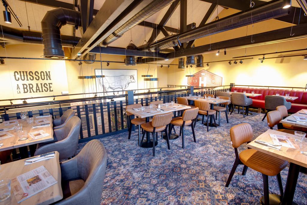 Restaurant Hippopotamus spacieux avec tables en bois, chaises rembourrées, banquettes rouges et décorations murales. Les poutres apparentes et la moquette à motifs complètent le décor.