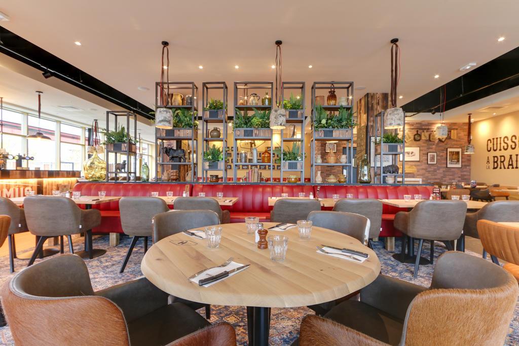Intérieur de restaurant Hippopotamus moderne avec banquettes rouges, tables en bois, chaises assorties, suspensions lumineuses et étagères décoratives pour plantes. Touches rustiques partout.