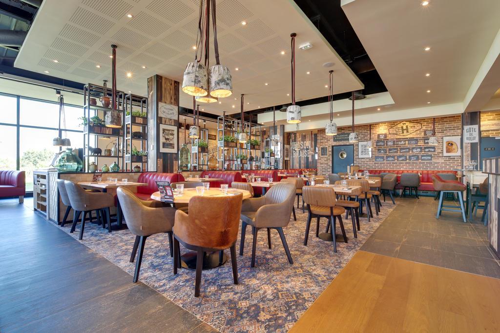 Intérieur moderne d'un restaurant Hippopotamus avec tables en bois, chaises assorties, suspensions lumineuses et fenêtres laissant entrer la lumière naturelle. Ambiance chaleureuse et élégante.
