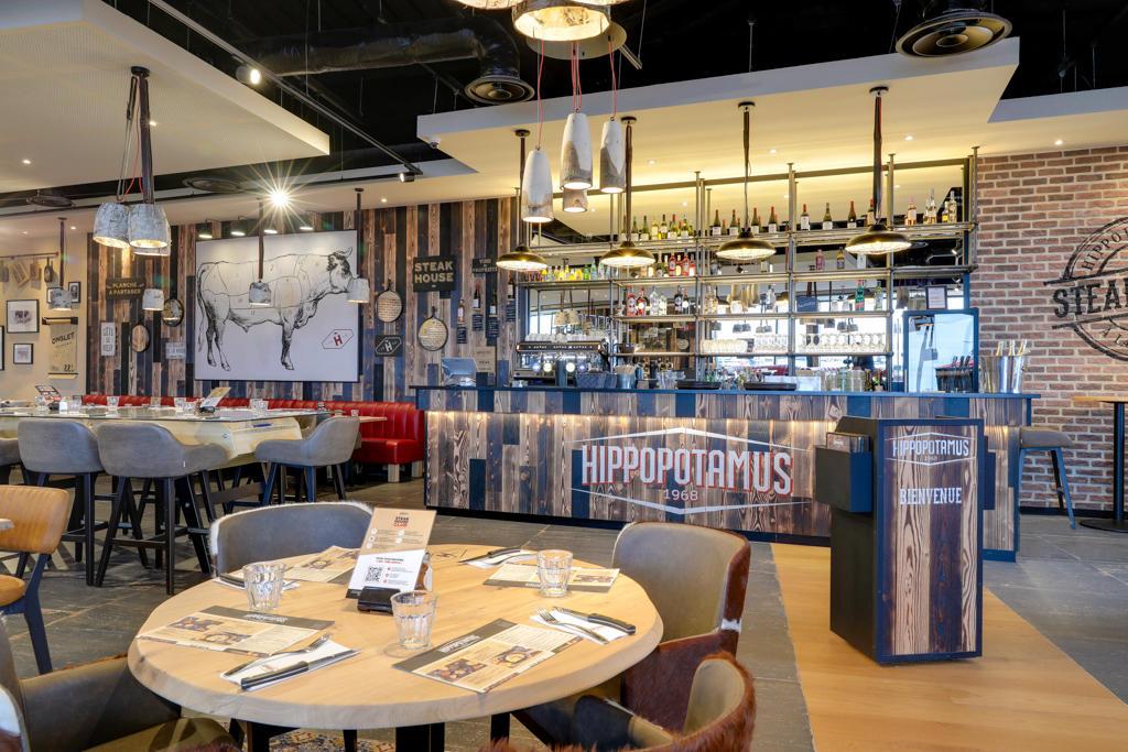 Intérieur moderne d'un restaurant Hippopotamus avec un bar en bois, entouré de tables, de chaises et de décorations murales. Atmosphère chaleureuse et accueillante.