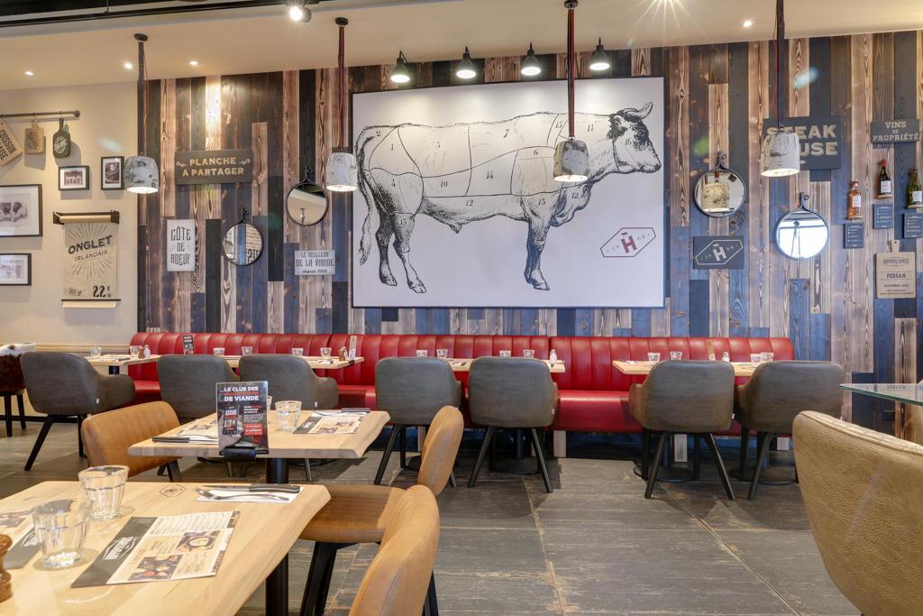 Intérieur d'un restaurant Hippopotamus avec des banquettes rouges, des murs en bois ornés d'un diagramme représentant une vache et une décoration vintage, ainsi que des tables dressées avec des menus et des verres.