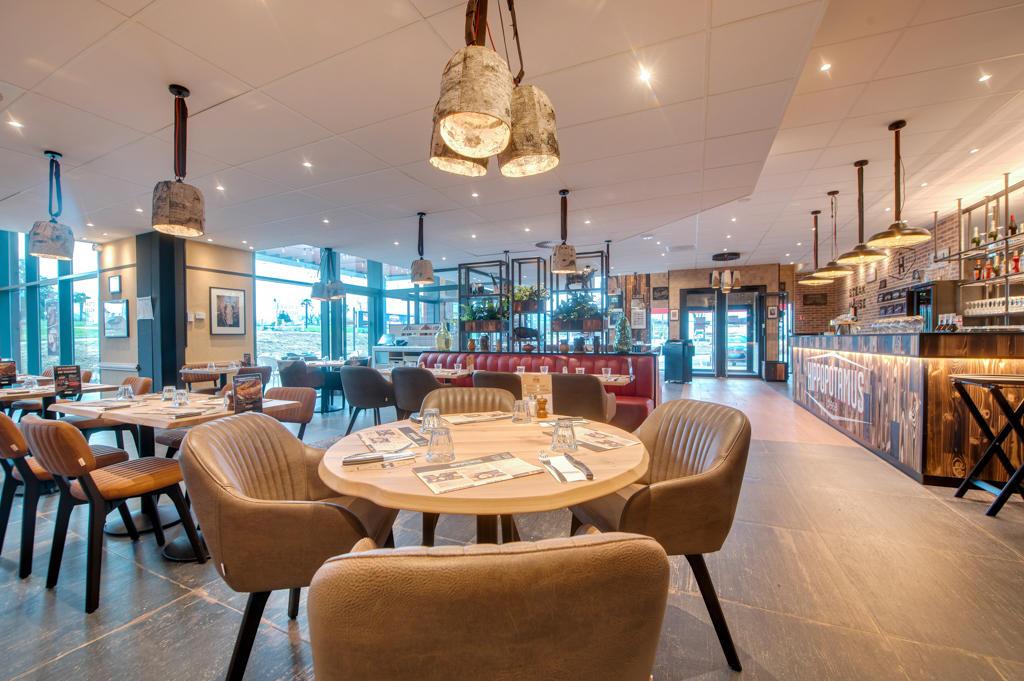 Intérieur chaleureux d'un restaurant Hippopotamus avec des sièges rembourrés rouges, des tables en bois, des plantes, des objets décoratifs et de grandes fenêtres donnant sur l'extérieur.