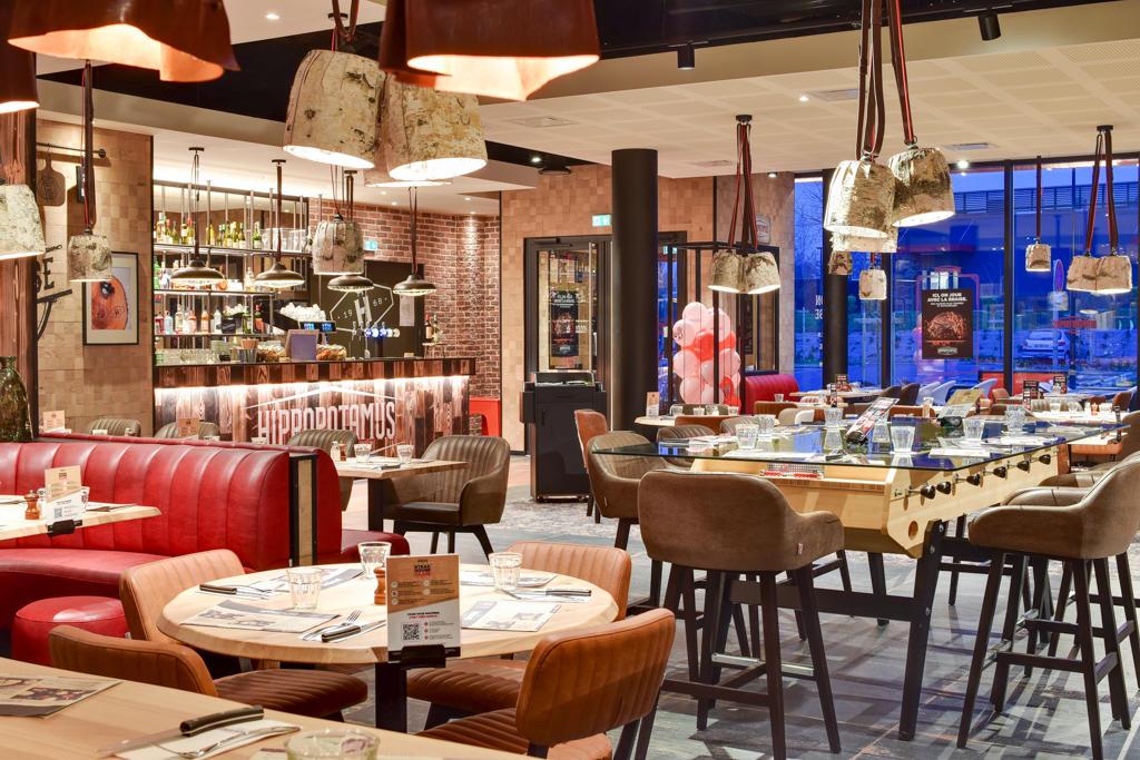 Un restaurant Hippopotamus moderne avec des banquettes en cuir rouge, des tables en bois, un bar bien approvisionné et un éclairage d'ambiance, créant une atmosphère chaleureuse.