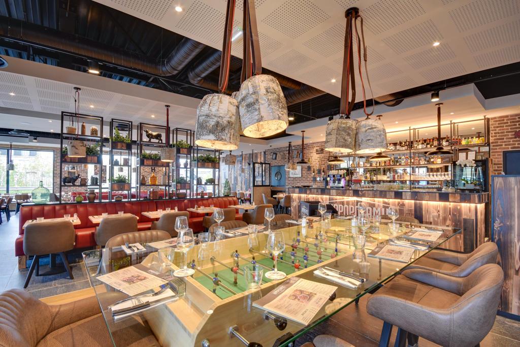 Restaurant Hippopotamus moderne avec une table de baby-foot servant de table à manger, des chaises en cuir, des banquettes rouges et des murs en briques apparentes, créant une ambiance élégante.