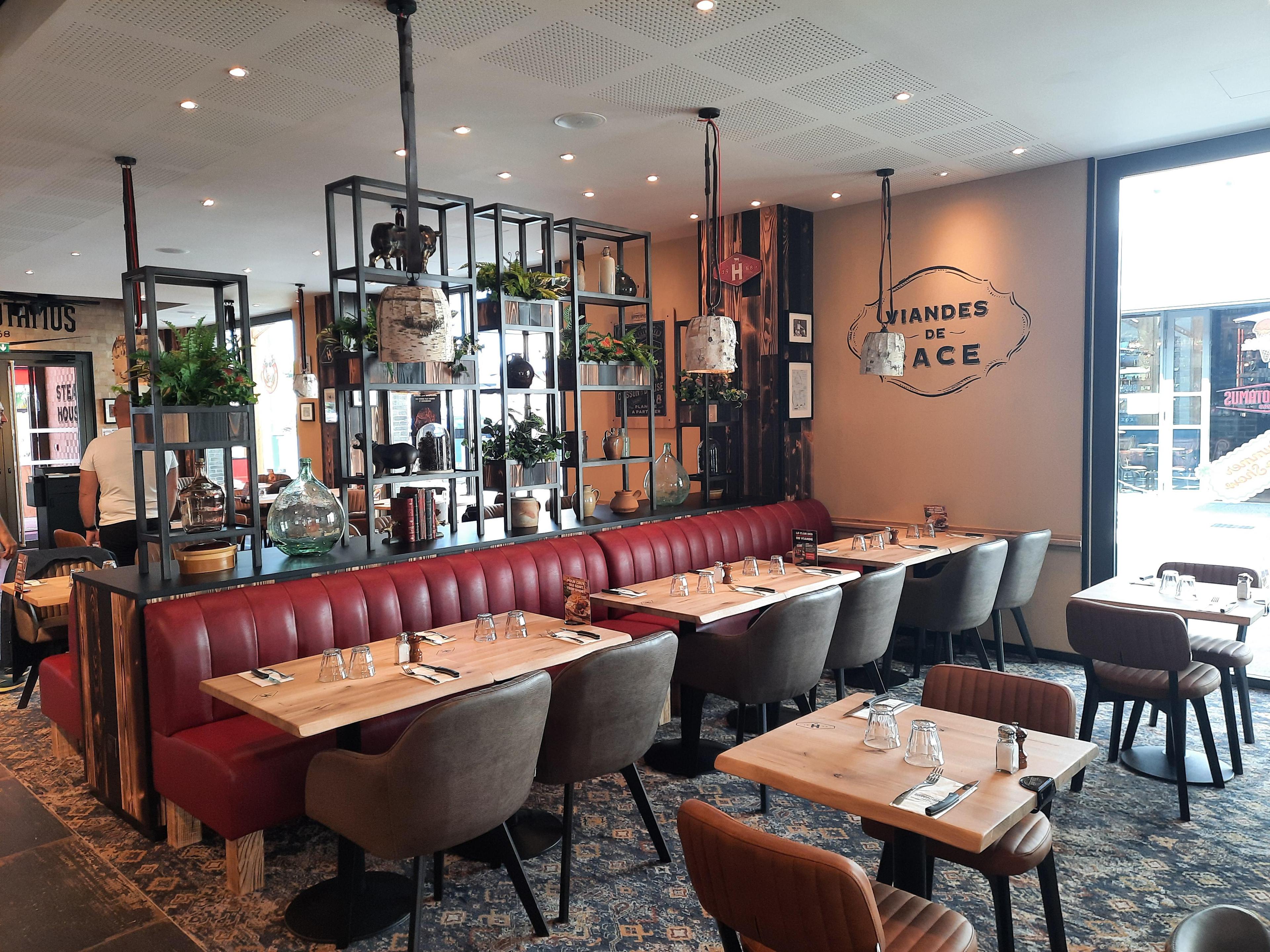 Restaurant Hippopotamus confortable avec des banquettes rouges, des tables en bois ornées de verres, une décoration moderne et des plantes suspendues, créant une ambiance chaleureuse.