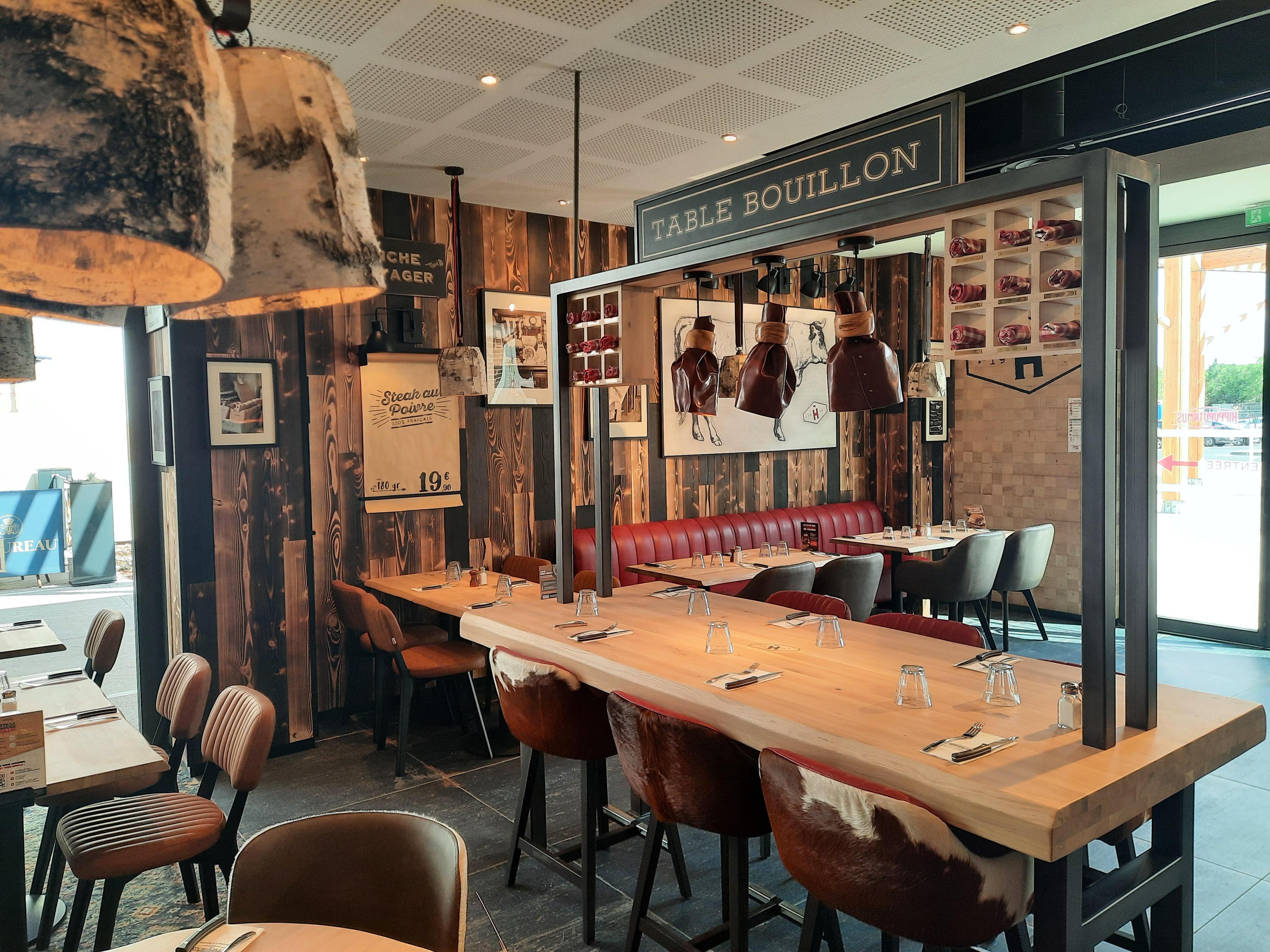 Intérieur chaleureux d'un restaurant Hippopotamus avec décor en bois, tables dressées avec verres et couverts, chaises en cuir et décorations murales artistiques.