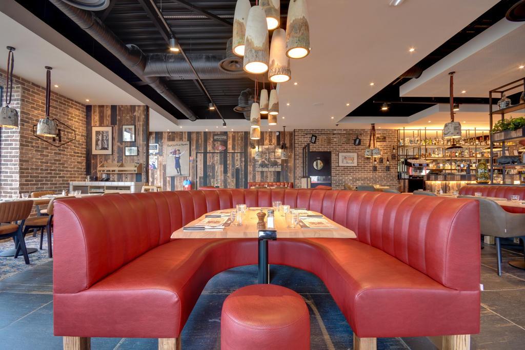 Restaurant Hippopotamus spacieux avec banquettes en cuir rouge, tables en bois, murs en briques et luminaires suspendus modernes.