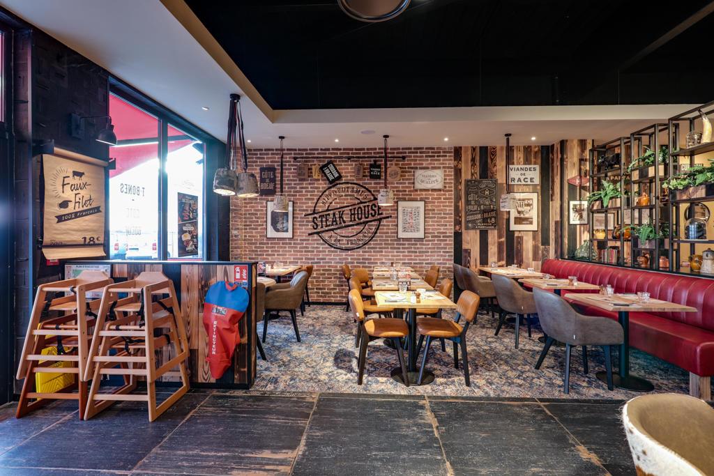 Intérieur chaleureux de steakhouse avec banquettes rouges, tables en bois, décor mural et accents en bois massif, créant une ambiance chaleureuse et accueillante.