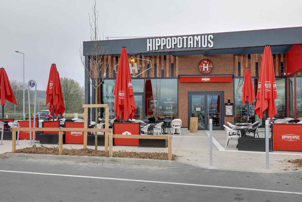 Restaurant Hippopotamus avec une façade moderne, des parasols rouges et des tables en terrasse le long d'une rue.