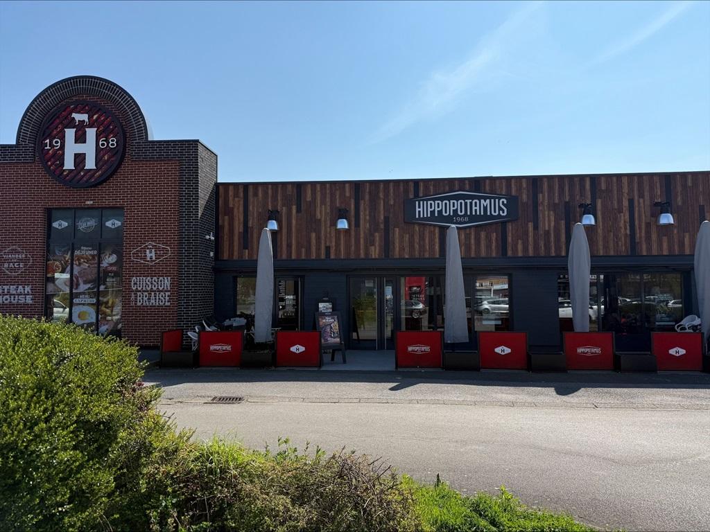 Extérieur d'un restaurant Hippopotamus avec une façade en brique et en bois, un grand logo et des tables en terrasse sous des parasols par une journée ensoleillée.